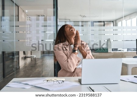 Euphoric professional young African American business woman executive feeling happy about financial work results, corporate goals achievement getting new job offer sitting with laptop in office.