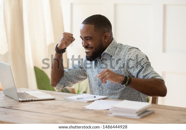Euphoric young black man celebrating online\
lottery win, excellent educational online courses tests results,\
successful qualification training, getting remote dream work,\
received high paid job\
offer.