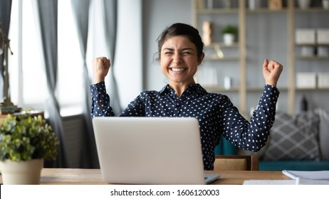 Euphoric Young Indian Girl Student Winner Celebrate Victory Triumph Sit At Home Desk With Laptop Computer Win Online Fortune Feel Excited Get New Job Opportunity Good Exam Result Great News Concept