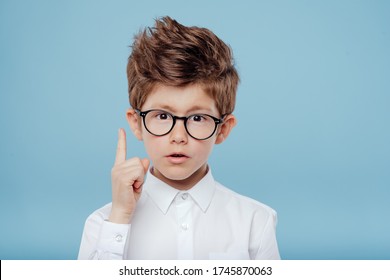 eureka, handsome little boy in glasses is surprised, inspired, I have an idea, Raise your index finger up, copy space, isolated on blue background