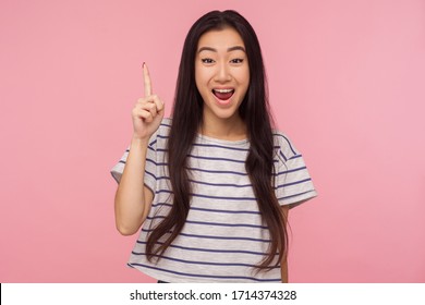 Eureka! Portrait Of Inspired Girl With Long Hair In Striped T-shirt Pointing Finger Up With Genius Idea, Surprised By Suddenly Invented Smart Solution. Indoor Studio Shot Isolated On Pink Background