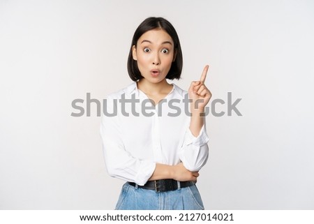 Eureka. Young smart asian girl has an idea, raising finger up, sharing her plan, pointing on top, standing over white background