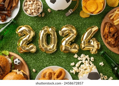 Euro 2024 soccer viewing setup. Top view shot of 2024-shaped balloons, party snacks like chips, nuts, fried chicken, onion rings, popcorn, chips, beer bottles, football, referee whistle on grass field - Powered by Shutterstock