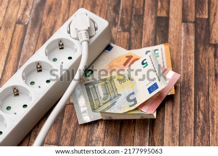 Euro banknotes next to a power socket. Symbolic image for a high electricity price. Increasing energy costs due to inflation effects. Multi plug socket in a domestic environment.