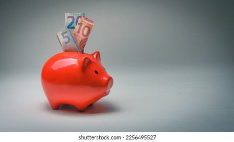 Euro banknotes are put into a red piggy bank to save - Shutterstock ID 2256495527