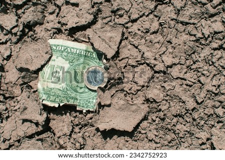 A euro coin and a battered dollar lie on the drought-cracked earth