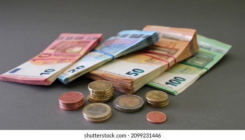 Euro coins and stacks of 10, 20, 50 and 100 euro banknotes, tied with rubber band, isolated on a grey background. Euro money. Close up view.