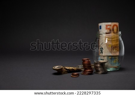 Euro money coins and banknote on a dark background saving concept. Fifty euro banknote inside a glass jar with stacked euro coins on the side. Copy space.
