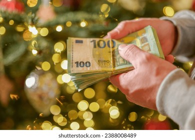 euro money in hands on a Christmas trees background.Christmas and New Year expenses. Spending on gifts and Christmas decor.Expenses during the winter holidays