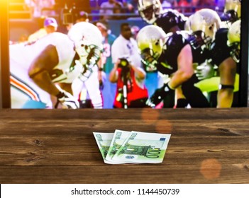 Euro Money On The Background Of A TV On Which American Football Is Shown, Betting On Sports, Euro And American Football