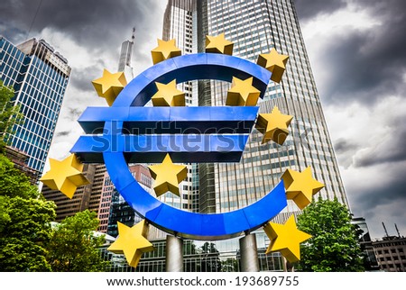 Euro sign at European Central Bank headquarters in Frankfurt, Germany with dark dramatic clouds symbolizing a financial crisis