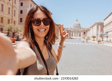 Europe luxury travel vacation tourist in Rome, Italy. Cheerful woman taking selfie photo with phone doing v sign with fingers at Vatican city St Peter's Basilica church. Summer holiday destination.