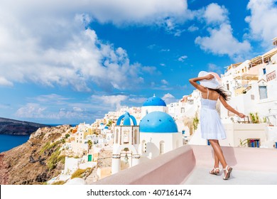 Europe Tourist Travel Woman In Oia, Santorini, Greece. Happy Young Woman Looking At Famous Blue Dome Church Landmark Destination. Beautiful Girl In White Dress On Visiting The Greek Island.