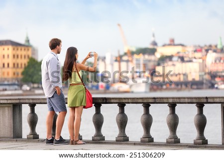 Europe travel tourist people taking pictures. Tourists couple in Stockholm taking smartphone photos having fun enjoying skyline view and river by Stockholm's City Hall, Sweden.