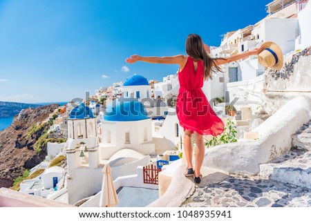 Europe travel vacation fun summer woman dancing in freedom with arms up happy in Oia, Santorini, Greece island. Carefree girl tourist in European destination wearing red fashion dress.