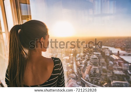 Europe travel woman looking at sunset view of London city skyline from the window of highrise skyscraper tower, famous tourist attraction in the U.K.