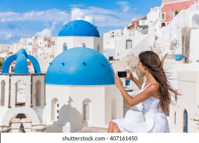 Europe Travel Woman Taking Photo Photographing Using Smart Phone In Oia, Santorini, Greece. Famous Blue Domes On White Church In Village. Young Asian Tourist Taking Pictures On Smartphone On Holidays