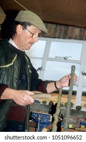 Europe UK Bedfordshire Kempston 2000. Caucasian Older Man Inside His Workshop. Holding A Short Stick Ready To Carve Into Wooden Walking Stick Using Workbench Tools.