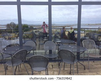 Europe UK Norfolk Burnham Deepdale October 2017. Ladies Sitting On Terrace Of A Restaurant. Chatting, Looking  To The Sea. Lady With IPhone Taking Selfie Photo Of Herself And Friends In Window Glass