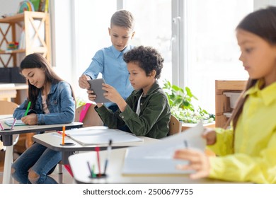 European and African American boys using tablet device in classroom, playing games during break. Technologies and education concept - Powered by Shutterstock