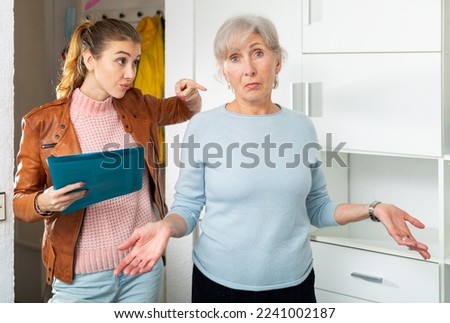 European aged woman and young woman discussing breach of rent contract at home. Senior woman showing helpless gesture.
