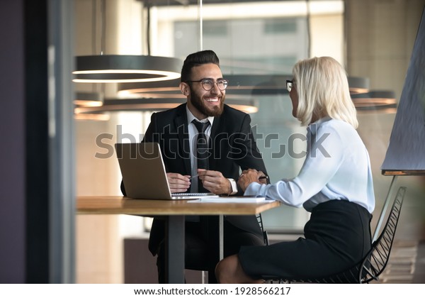 European Arabian business partners negotiating\
sit at desk hold pens pc notepads on table, diverse client and boss\
meet for solve issues, plan future cooperation, making profitable\
proposition concept
