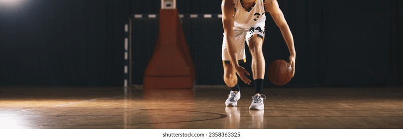 Jugador de baloncesto europeo lanza una bola contra una cancha de madera. El atleta Dribel Basketball en la unidad de entrenamiento