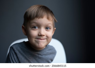 European Boy, Blond, Preschooler Surprised. Self Haircut, Curved Hair Bangs. Portrait On A Gray Background. Sly Look, Emotions, Model.