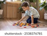 A European boy lays out a circular mandala pattern from wooden geometric figures. A child is concentrating on assembling a flower from a construction set on the floor.