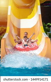 European boy and mom gliding down slide in waterpark. They enjoy the fun and holding hands wide open.
