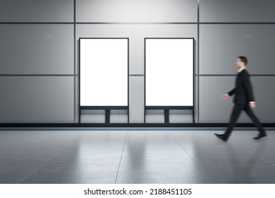 European businessman walking past two empty white banners in underground corridor. Mock up