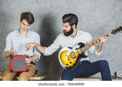 European Businessmen Playing With Guitar In Office Interior With Desk And Concrete Wall Background. Leisure, Music, Rehearsal, Band Concept