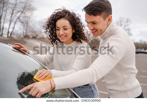 European couple\
cleaning car windshield with\
rag