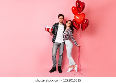 European Couple Posing In Anniversary. Studio Full Length Shot Of Man Embracing Wife And Holding Present.