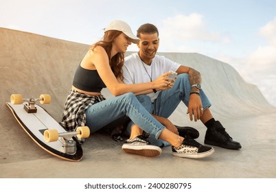 European couple sitting on skateboarding ramp, using phone and surfing internet, searching trick tutorial, free space. Happy skaters man and woman resting with cellphone - Powered by Shutterstock