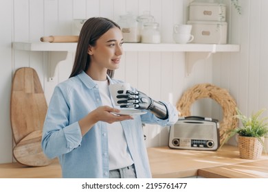 European Disabled Girl Is Holding Cup With Cyber Hand. Woman Has Tea At Domestic Kitchen. Concept Of Grasp Sensors In Modern Bionic Prosthesis. Technologies And Innovations For Life Quality.