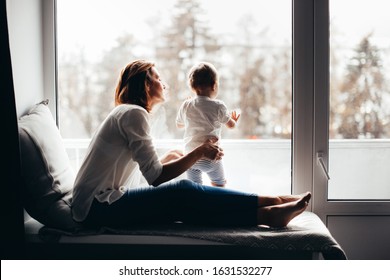 European Family, Mom With Baby Toddler At The Window In The Evening. Mood Slow Life Lifestyle In A Real Interior