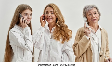 European Family Of Three Female Generations Talking On Old And New Smartphones And Landline Phone. Age And Generation Concept. Grandmother, Mother And Granddaughter. White Background. Studio Shoot