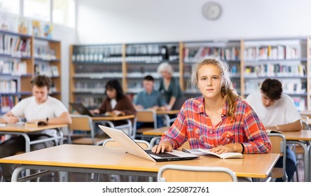 European fifteen-old-year schoolgirl, preparing for classes in the school library searches for information on a laptop and writes a abstract in a copybook
