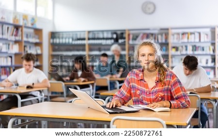 European fifteen-old-year schoolgirl, preparing for classes in the school library searches for information on a laptop and writes a abstract in a copybook