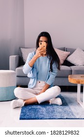 European Fit Brunette Fashion Blogger Woman Sits On Floor In Living Room Near Sofa, Wearing White Jeans And Blue Sweather, And Take Photo Selfie In Mirror