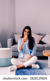 European Fit Brunette Fashion Blogger Woman Sits On Floor In Living Room Near Sofa, Wearing White Jeans And Blue Sweather, And Take Photo Selfie In Mirror