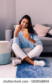 European Fit Brunette Fashion Blogger Woman Sits On Floor In Living Room Near Sofa, Wearing White Jeans And Blue Sweather, And Take Photo Selfie In Mirror   