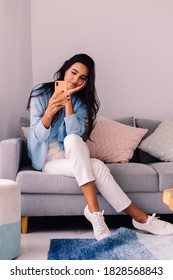 European Fit Brunette Fashion Blogger Woman Sits On Floor In Living Room Near Sofa, Wearing White Jeans And Blue Sweather, And Take Photo Selfie In Mirror   