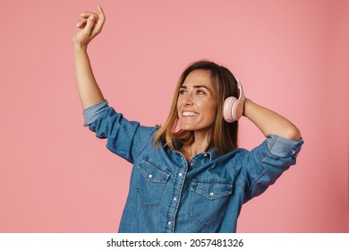 European Ginger Woman Dancing While Listening Music With Headphones Isolated Over Pink Background