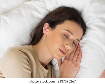 European Girl Getting Ready For Bed. A Pink Earplug In Your Ear Will Give You Peace And Quiet All Night Long. Woman On A Pillow In The Bedroom.