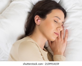 European Girl Getting Ready For Bed. A Pink Earplug In Your Ear Will Give You Peace And Quiet All Night Long. Woman On A Pillow In The Bedroom.