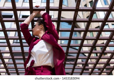 European Girl With Short Haircut Poses Cool In A Red Jacket. Women's Pantsuit Burgundy Color On The Model. Street Photo Lifestyle.