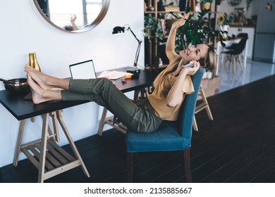 European girl talking on mobile phone at home. Concept of modern woman. Idea of remote or e-learning. Young smiling woman sitting in armchair at desk with opened laptop. Interior of studio apartment