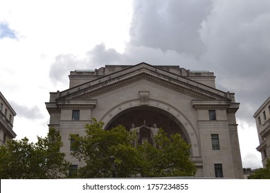 European Greek revival architecture with statues, fronted by trees and with a stormy sky backdrop. 